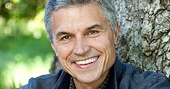 Older man smiling outdoors in front of tree