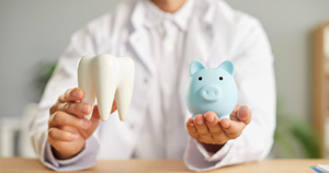 Dentist holding tooth model and piggy bank
