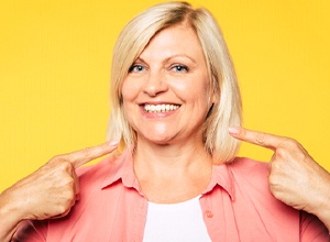 Woman standing against yellow background, enjoying benefits of implant dentures