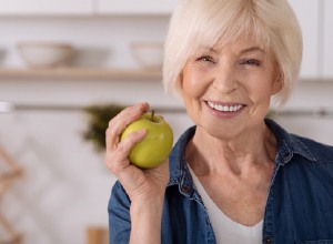 Smiling woman with dental implants in Meriden holding an apple