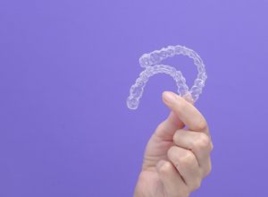 Hand holding two clear aligners against purple background