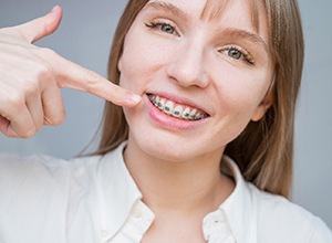 Young woman in white blouse pointing at her traditional braces