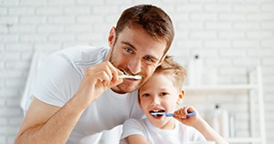 Father and son, wearing white shirts and brushing teeth together