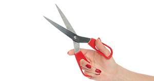 Woman’s hand with painted fingernails holding scissors against white background