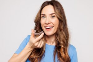 Smiling woman holding Invisalign aligner 