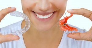 Woman holding a Hawley retainer and a clear plastic retainer in Meriden