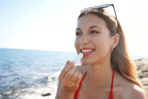 Woman outside on beach, applying lip balm